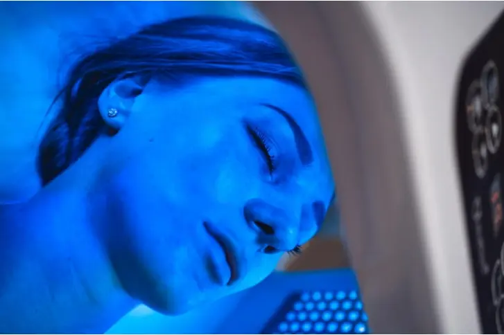 Imagem de uma mulher recebendo terapia capilar com LED azul, mostrando o dispositivo de tratamento em uso.